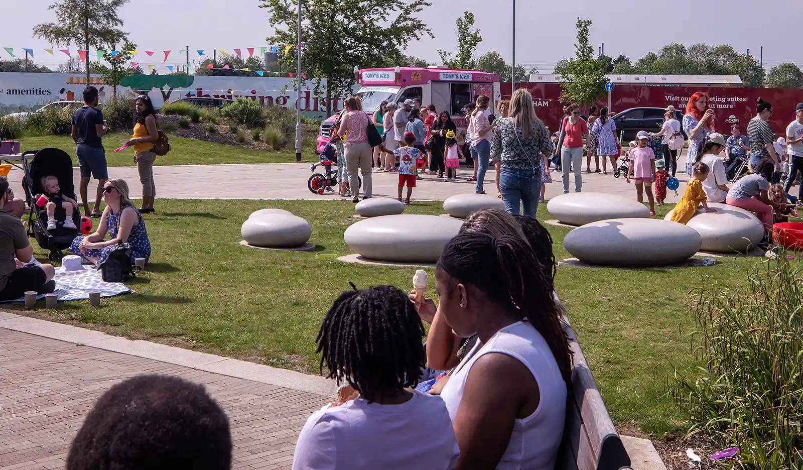 Families sitting outside in the sun with an ice cream van in the background