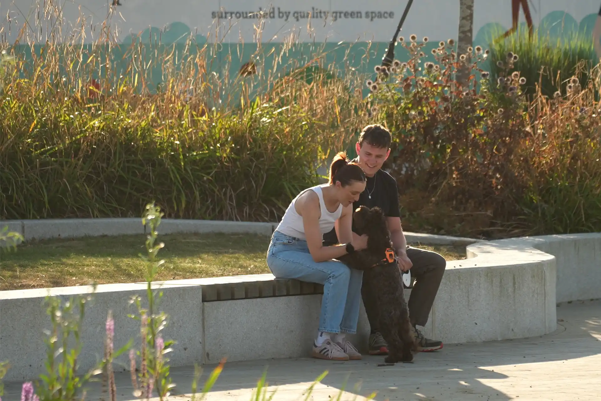 A young man and woman sitting in a park, fussing a dog